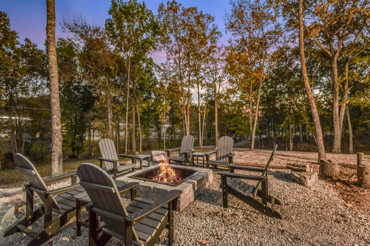 A cozy outdoor fire pit area is surrounded by classic Adirondack chairs, set against a backdrop of lush trees. The scene exudes a relaxed, communal vibe, perfect for families to gather and share stories or roast marshmallows after a day out exploring local attractions.