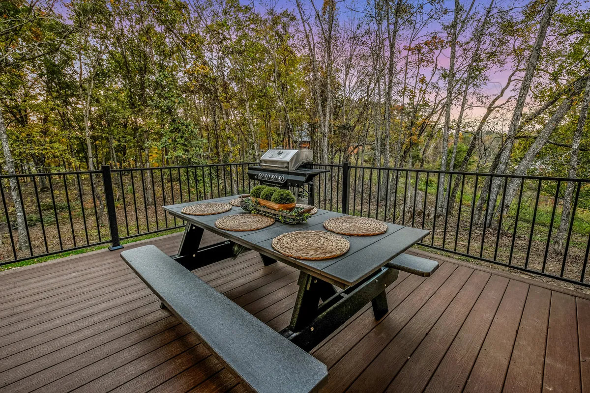 A picnic table and propane grill are set on the wooden deck, embraced by a lush natural background. The setup is ready for outdoor dining, barbecues, or peaceful morning coffees, inviting guests to enjoy meals in the open air.