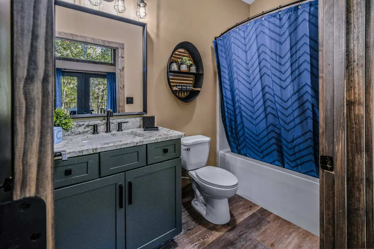 A refreshing bathroom scene with a vanity featuring a granite countertop, a blue shower curtain, a framed mirror, and shelf with rolled towels. The mood is calm and inviting, ideal for self-care.
