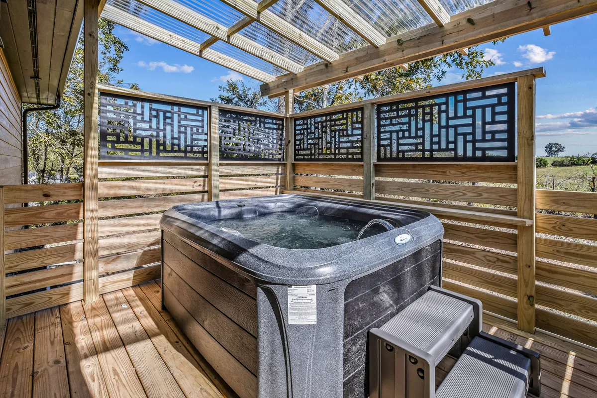 This image features a covered hot tub set on a wooden deck, with decorative privacy screens and a view of the sky beyond. The setting is surrounded by trees, offering both seclusion and a tranquil natural backdrop ideal for relaxing soaks.