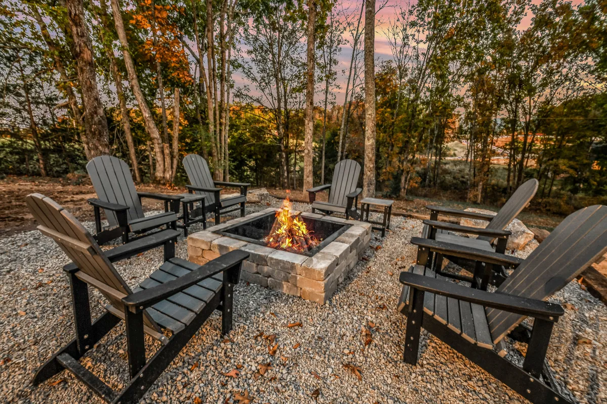 A classic fire pit surrounded by Adirondack chairs is nestled among trees. The scene suggests an inviting evening gathering space, perfect for storytelling, roasting marshmallows, and stargazing under the open sky.